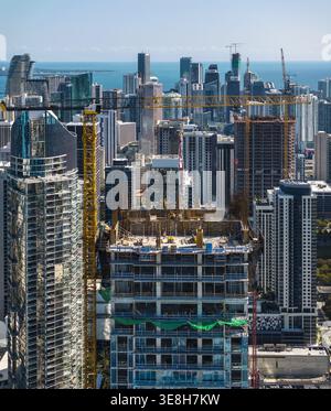 Vue aérienne de gratte-ciels scintillants perçant le ciel Azur, grues de construction peignant des traits jaunes sur la toile urbaine, Miami, Floride, États-Unis Banque D'Images