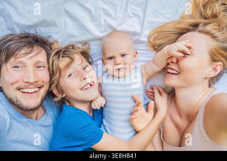 Bébé allongé sur le lit avec la mère, le père et le frère aîné à la maison. Famille heureuse passer du temps ensemble, se lier et se détendre. Parentalité, frère ou sœur Banque D'Images