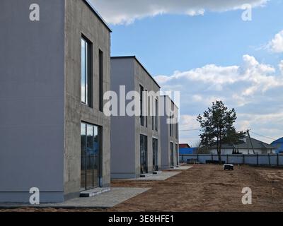 Rangée de bâtiments résidentiels à plusieurs étages inachevés faits de blocs de béton blanc sur un chantier de construction sous un ciel bleu avec des nuages. Banque D'Images