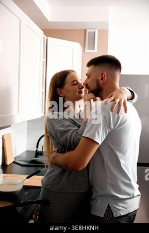 Un couple profite d'un moment proche dans la cuisine. Ils préparent la nourriture ensemble tout en souriant et en s’engageant les uns avec les autres. Le réglage est lumineux et Banque D'Images