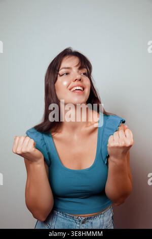Une femme aux cheveux longs sourit brillamment tout en faisant des gestes ludiques de la main. Portrait de femme jouit d'un moment de plaisir et de célébration en vêtements décontractés Banque D'Images