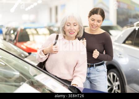 La fille adulte aide sa mère âgée à choisir une nouvelle voiture chez un concessionnaire automobile. Banque D'Images