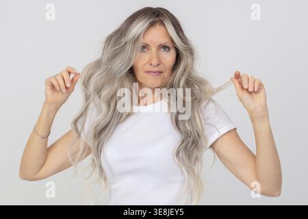Une femme âgée aux cheveux gris dans un débardeur blanc. Une dame âgée avec de longs cheveux sur un fond blanc Banque D'Images
