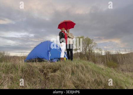 Un couple âgé se tient sous un parapluie près d'une tente touristique sous la pluie. Voyage d'un homme et d'une femme âgés dans la nature Banque D'Images