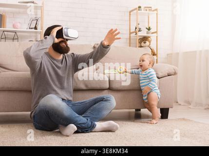 Père utilisant un casque de réalité virtuelle, assis avec bébé Banque D'Images