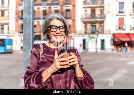 Femme mature souriant tenant la tasse de café à l'extérieur Banque D'Images