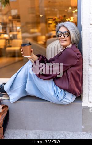 Femme élégante profitant d'une pause café dans la rue de la ville Banque D'Images
