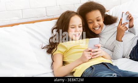 Enfants jouant à des jeux sur les téléphones, couchés sur le lit Banque D'Images