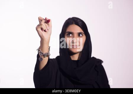 Jeune femme en hijab écrivant avec un marqueur rouge tout en regardant réfléchi et concentré Banque D'Images