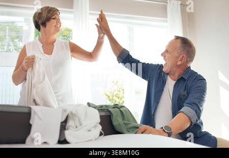 Aide, haut cinq et couple mature avec la lessive dans la chambre à coucher pour plier, ranger et trier les vêtements ensemble. Mariage, heureux et homme avec femme avec Banque D'Images