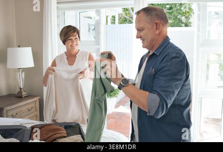 Aide, couple heureux et mature avec la lessive dans la chambre à coucher pour plier, corvées et trier les vêtements ensemble. Mariage, maison et homme avec femme avec Banque D'Images