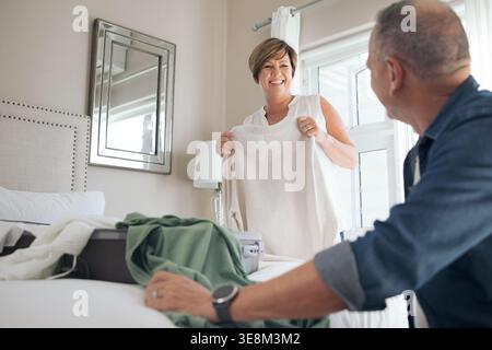 Aide, maison et couple mature avec la lessive dans la chambre à coucher pour plier, ranger et trier les vêtements ensemble. Mariage, retraite et homme avec femme avec Banque D'Images