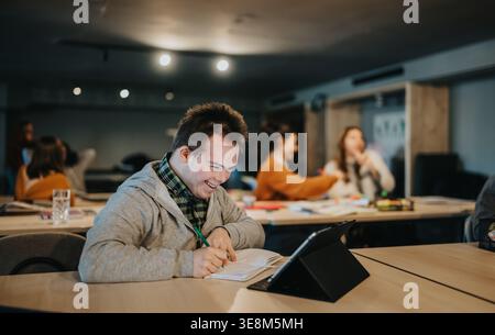 Étudiant souriant atteint de trisomie 21 étudiant avec tablette dans une classe inclusive Banque D'Images