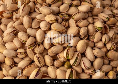 Gros plan détaillé d'un groupe de pistaches, mettant en évidence les textures naturelles des coquilles et les couleurs vibrantes des viandes de noix exposées. Banque D'Images