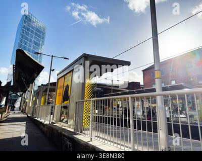 Manchester, Royaume-Uni - 22 février 2026 : plate-forme de tramway ensoleillée et tour de verre moderne à Manchester Royaume-Uni, mettant en valeur le transport urbain et l'architecture. Banque D'Images