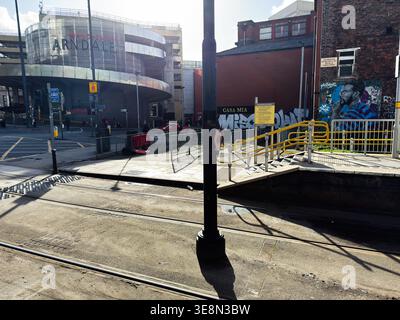 Manchester, Royaume-Uni - 22 février 2026 : rue urbaine ensoleillée et voies de tramway à l'extérieur de Manchester Arndale avec graffitis muraux et piétons. Banque D'Images