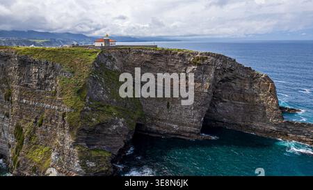 Une vue aérienne majestueuse capture le phare de Cabo vidio perché sur d'imposantes falaises surplombant la mer Cantabrique. L'architecture à toit rouge contr Banque D'Images