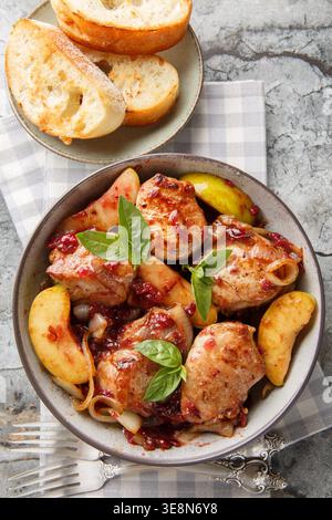 Tranches de filet de porc cuit avec pommes sautées, oignon et sauce aux airelles dans un bol en céramique servi avec du pain grillé en gros plan sur la table. Verti Banque D'Images