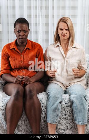 Deux femmes diverses bouleversées assises sur un canapé montrant des émotions négatives Banque D'Images