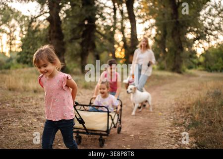 Des enfants heureux tirant un chariot avec leurs sœurs jumelles dans un chemin forestier Banque D'Images