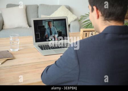 Jeune homme ayant un entretien d'embauche en ligne à la maison, vue arrière Banque D'Images