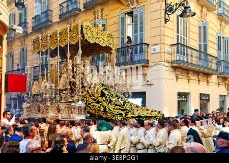 Un grand flotteur religieux se déplace dans les rues de Malaga pendant la semaine Sainte de Pâques. Beaucoup de gens regardent et participent à la procession. Banque D'Images