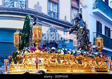 À Séville pendant la semaine Sainte, un flotteur en bois porte des figures religieuses. Les gens regardent la procession se déplacer dans les rues. Banque D'Images
