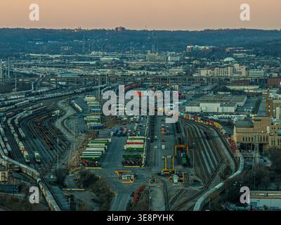 Cincinnati, États-Unis - 27 février 2026 : vue aérienne d'un vaste chantier de chemin de fer baigné dans la lueur chaude du soleil couchant, avec des trains serpentant sur la route Banque D'Images