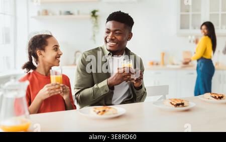 Les membres de la famille apprécient les boissons et le petit déjeuner ensemble dans un cadre lumineux de cuisine Banque D'Images