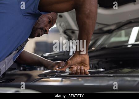 Un mécanicien qualifié se concentre sur la vérification et la réparation d'un moteur de voiture dans un garage. Banque D'Images