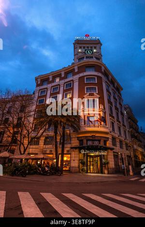 Bâtiment d'angle orné de briques rouges avec horloge sur le toit et entrée éclairée à l'aube Banque D'Images