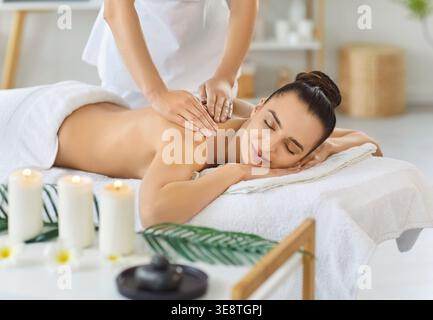 Femme souriante allongée sur la table de massage, appréciant le soin relaxant du dos et des épaules dans le salon de spa. Banque D'Images