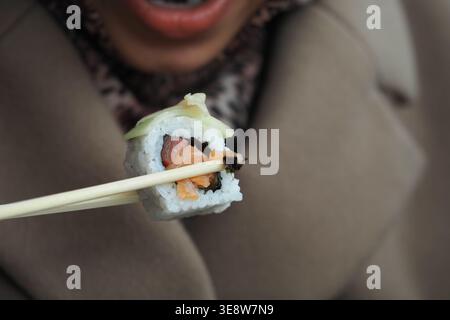 La personne tient des sushis avec des baguettes près de la bouche Banque D'Images