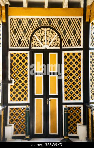 Une porte d'entrée traditionnelle en bois frappante avec des panneaux jaunes et noirs éclatants, des motifs floraux sculptés à la main complexes et de la quincaillerie en métal classique. Banque D'Images