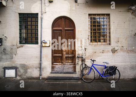 Un vieux vélo bleu appuyé contre un vieux mur de briques rouges et une porte à Livourne, en Italie Banque D'Images
