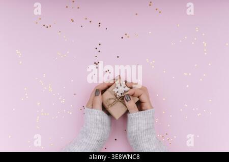 Un petit cadeau dans les mains d'une femme sur un fond rose élégant avec de l'éclat. Concept de Noël Banque D'Images