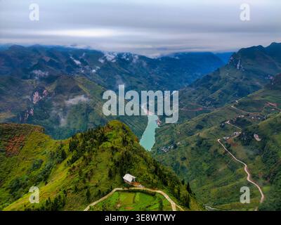 Vue aérienne de la boucle de Ha Giang avec la rivière turquoise Nho que serpentant à travers des montagnes vertes abruptes et des canyons brumeux avec une petite maison sur un Banque D'Images