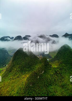 Vue aérienne des montagnes karstiques vertes luxuriantes partiellement couvertes par une brume blanche épaisse et des nuages bas sous un ciel couvert à Hoan Kiem, Ha Noi, Vietnam. Banque D'Images