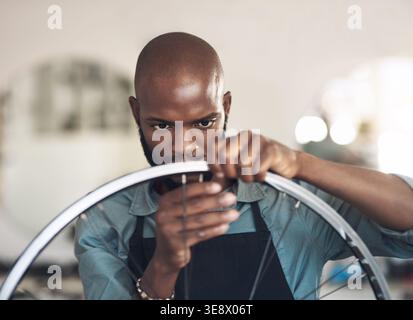 Fixation, roue et homme avec vélo en atelier, entrepreneur et sérieux pour l'entretien avec des outils. Mécanicien, garage et personne noire avec des compétences pour Banque D'Images