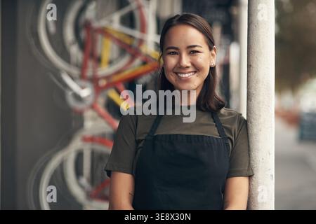 Mécanicien, portrait et femme heureuse dans un atelier de réparation de vélos, petite entreprise et entretien des transports. Confiant, entrepreneur et personne avec tablier pour Banque D'Images