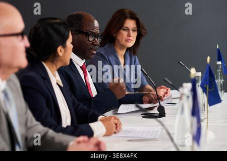 Des chefs d'entreprise multiethniques discutent de la politique lors d'un panel formel de conférence, avec un homme noir senior parlant dans le micro. Idéal pour la communication d'entreprise Banque D'Images