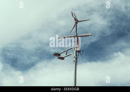 Vue rapprochée d’une éolienne et d’un panneau solaire montés sur un poteau, sur fond de ciel nuageux, représentant des solutions d’énergie renouvelable. Banque D'Images
