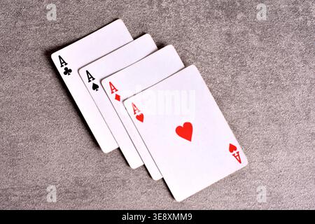 Gros plan en grand angle des quatre as d'un jeu de cartes standard, disposés en éventail sur une surface grise en pierre texturée. Banque D'Images