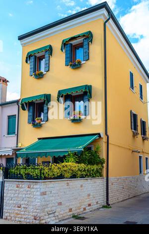 Bâtiment jaune vif avec auvents verts et jardinières, typique de l'architecture de Chioggia, sous un ciel bleu clair Banque D'Images