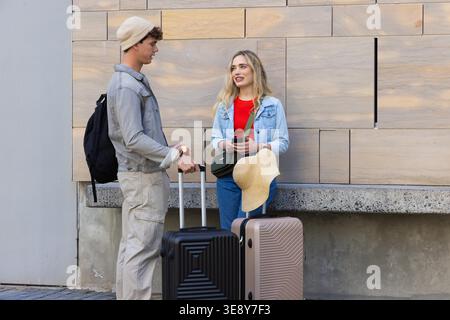 Couple debout par des panneaux de bois, en denim et vérification smartphone près du chapeau de paille et des valises. Bagages, voyageurs, urbain, transit, moderne, façade, couvert Banque D'Images