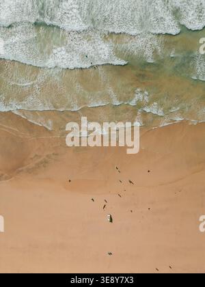 Vue aérienne de haut en bas par drone des vagues brisées sur le sable doré avec des personnages lointains sur la plage, côte nord de Cornwall près de Hayle, Angleterre, Royaume-Uni. Banque D'Images