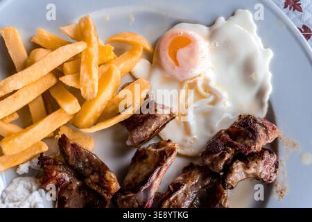 Côtes de porc grillées avec des frites dorées et un œuf frit sur une assiette blanche, repas de confort copieux servi en gros plan d'en haut Banque D'Images