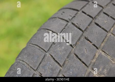 Un regard attentif à un pneu de voiture qui montre des signes d'usure. La bande de roulement du pneu présente des motifs et des marques clairs. Le pneu repose sur de l'herbe verte en plein jour Banque D'Images
