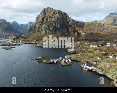 Vue aérienne des îles Lofoten avec des maisons traditionnelles en bois et une montagne rocheuse massive surplombant la mer calme Nordland, Norvège. Banque D'Images