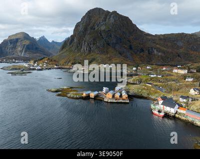 Vue aérienne des cabanes de pêche traditionnelles en bois et des montagnes escarpées le long de la côte rocheuse des îles Lofoten dans le Nordland, Norvège. Banque D'Images